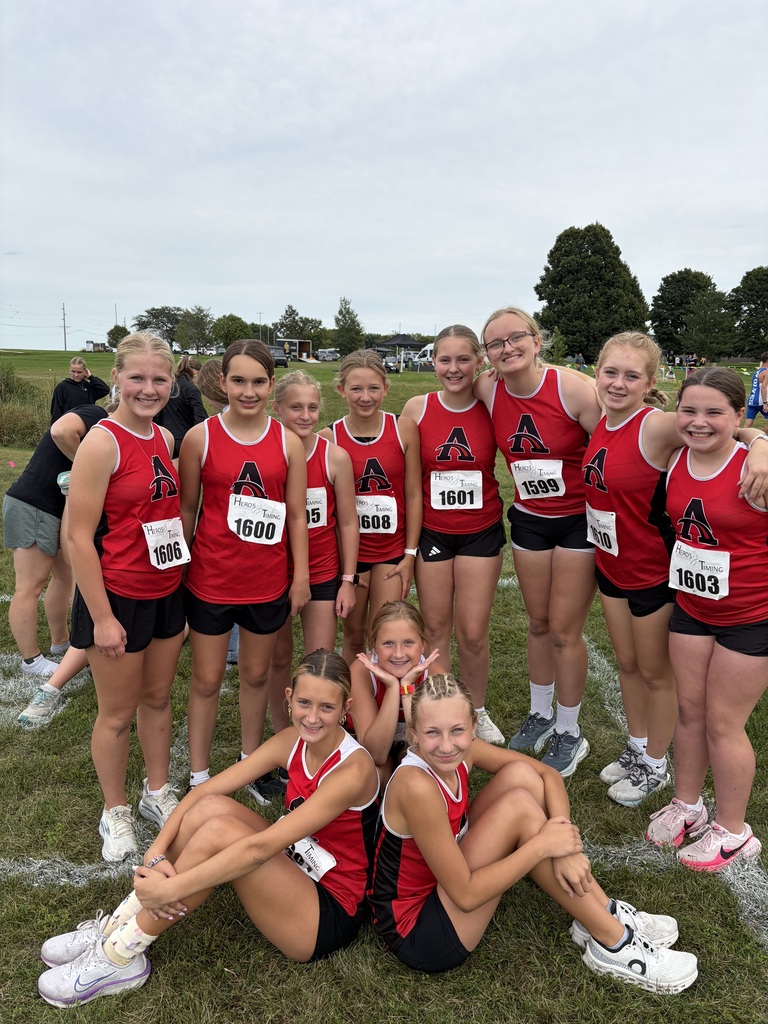 A group of young girls wearing red and black uniforms pose for a photo on a grass field.
