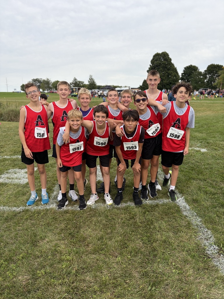 A group of young boys in matching red shirts and black shorts pose for a photo on grass.