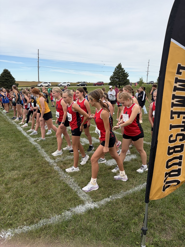 People in red shirts and black shorts line up on a grassy field for a race.