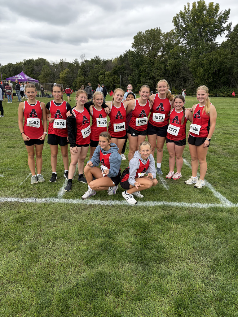 Group of female athletes in red and black uniforms pose for a photo on a grassy field.