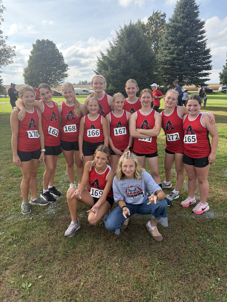 A group of young athletes in red and black uniforms pose for a photo in a park.