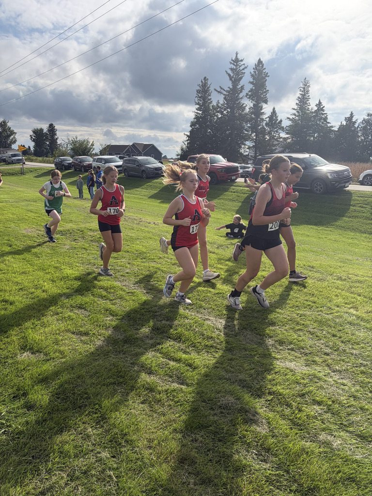 A group of athletes in red and green uniforms run in a race on a grassy field.