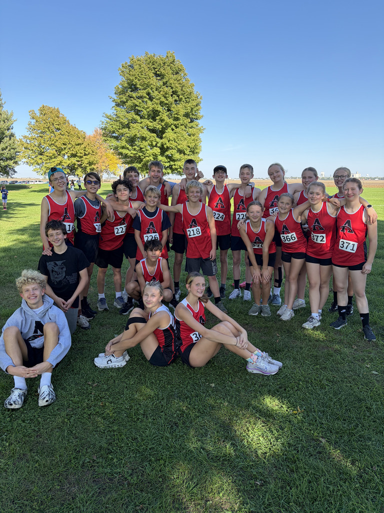 A group of runners dressed in red jerseys and shorts poses for a photo on a grassy field.