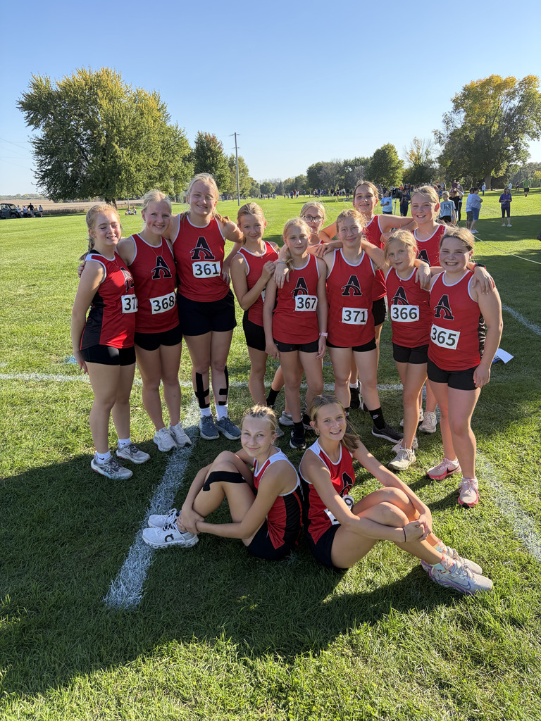 A group of young athletes in red and black uniforms poses for a photo on a grassy field.