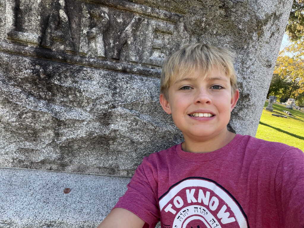 A young boy with short hair smiles in front of a concrete wall with a carved design.