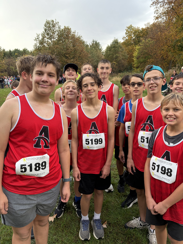 A group of young athletes in red shirts and numbers poses for a photo in a park.