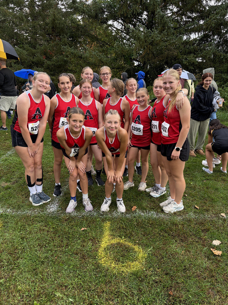 Group of young women in red athletic uniforms standing on a grassy field. Some wear black shorts, knee pads, and sneakers.