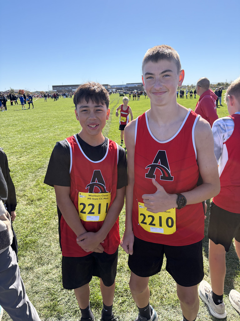 Two boys in red athletic shirts and black shorts pose for a photo at a sports event.
