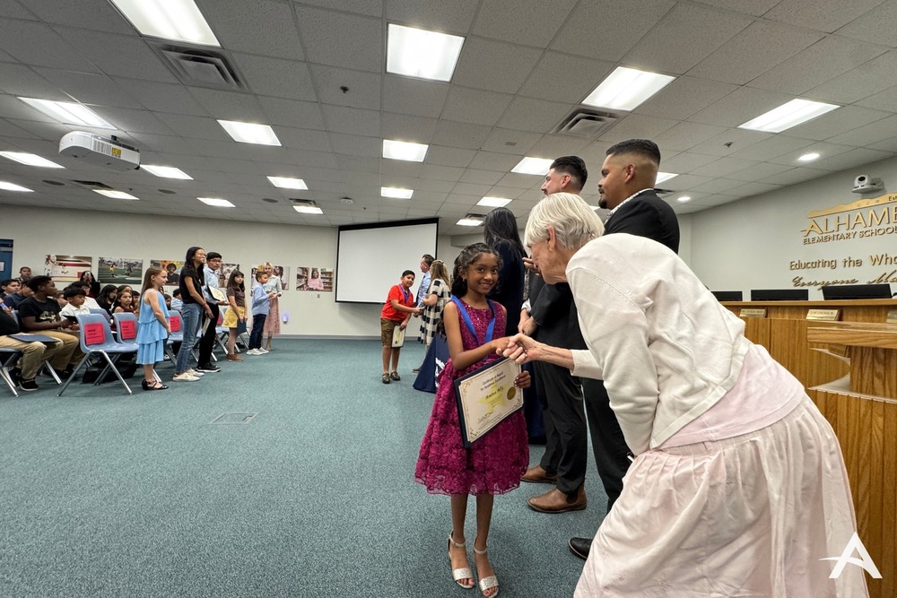 Female board member shaking hands with a young female student after receiving a medal and certificate