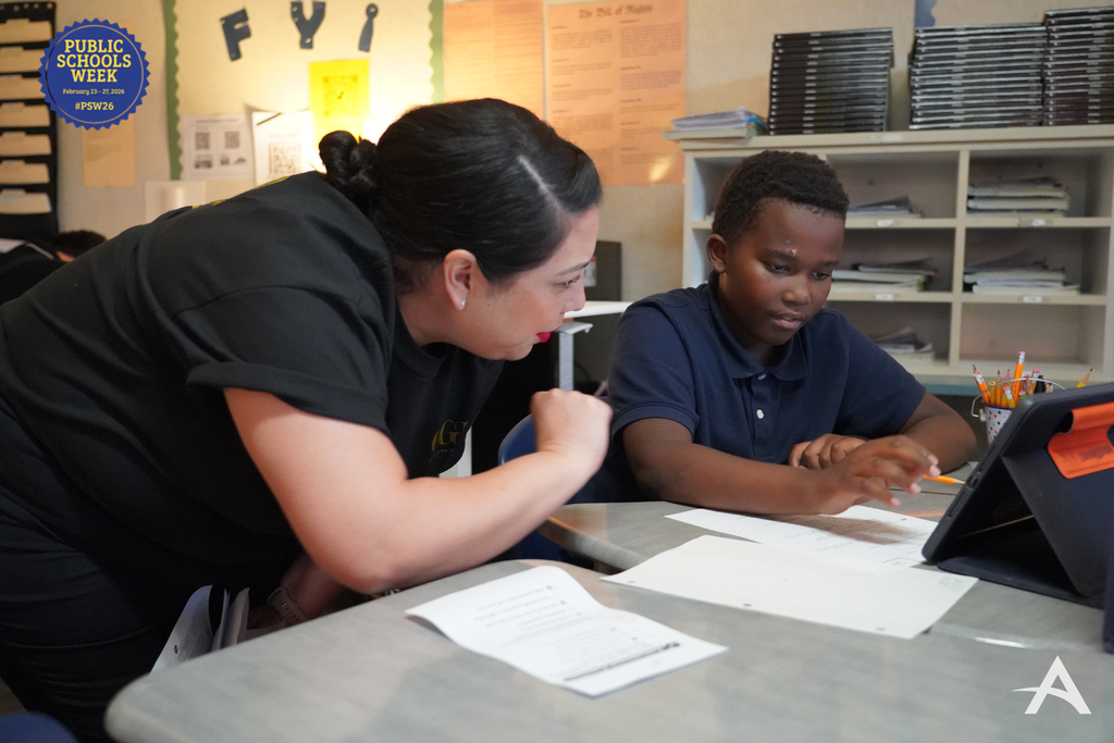 Teacher standing beside a student, reviewing the student’s work together on an iPad.