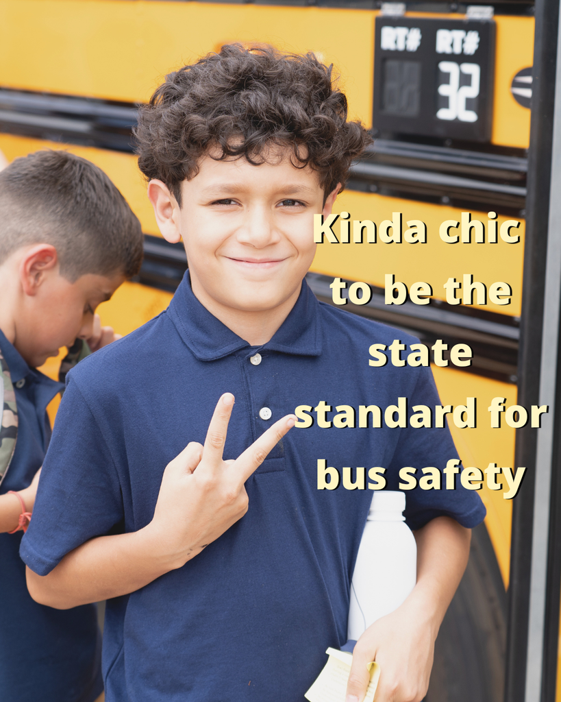 Image of a kid in front of a school bus holding up 2 fingers. Text overlayed on the image reads, "Kinda chic to be the state standard for bus safety"
