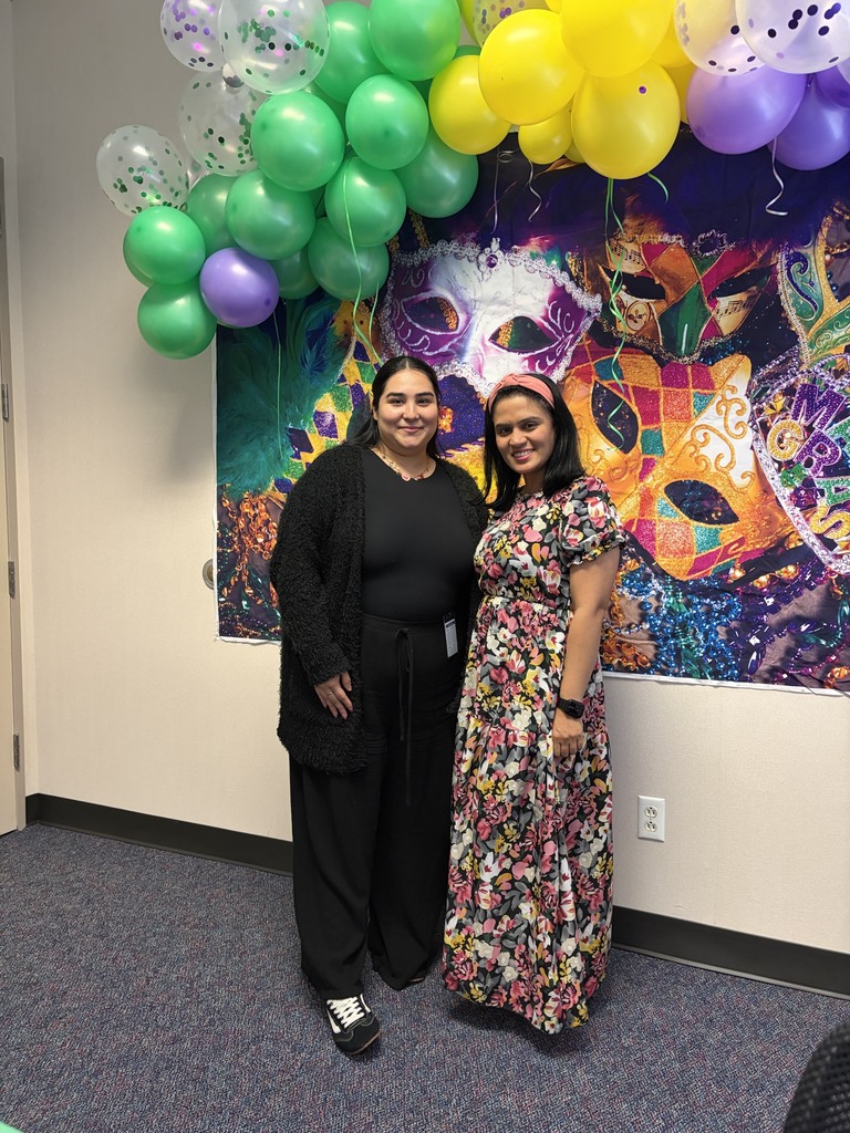 Two women in front of a colorful painting and balloons. One wears a floral dress and the other a black sweater.