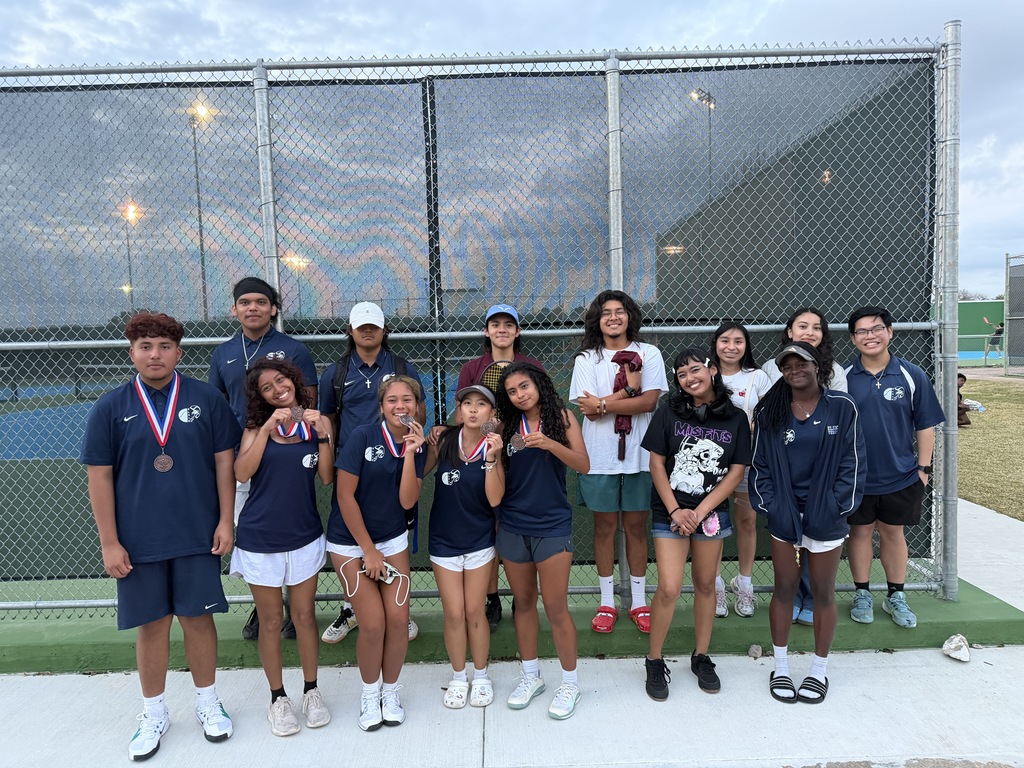 A group of tennis players wearing matching uniforms stand behind a fence on a tennis court.