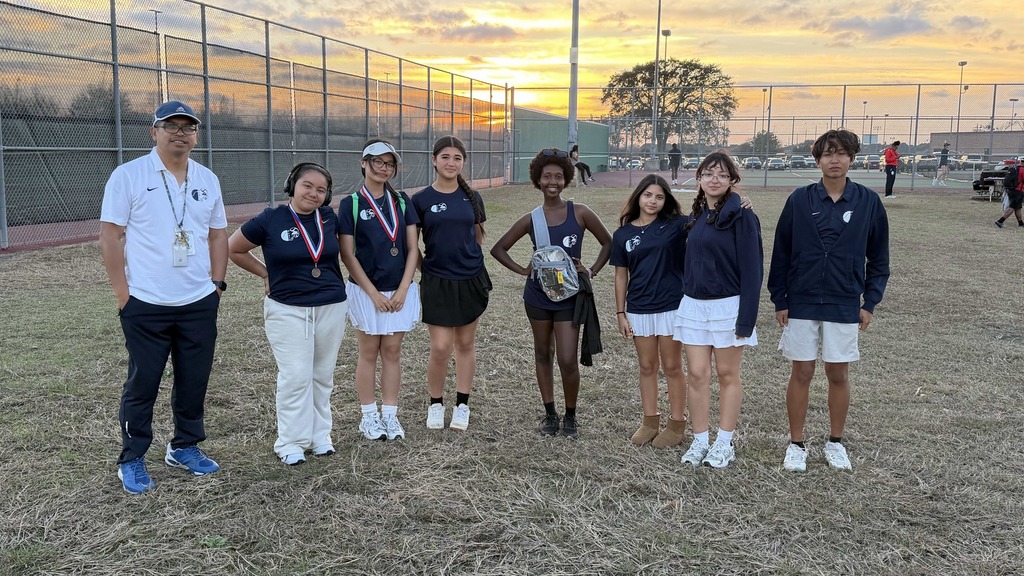 A group of athletes stands on a grassy field, holding medals, during a sunset.