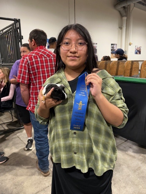Woman wearing glasses and a plaid shirt holding a small animal and a blue ribbon.