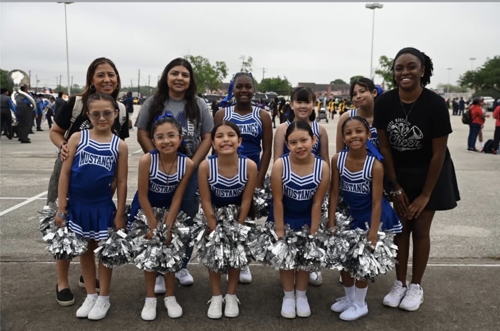 Cheerleaders in blue uniforms pose for a photo in an outdoor setting with a blurry background.