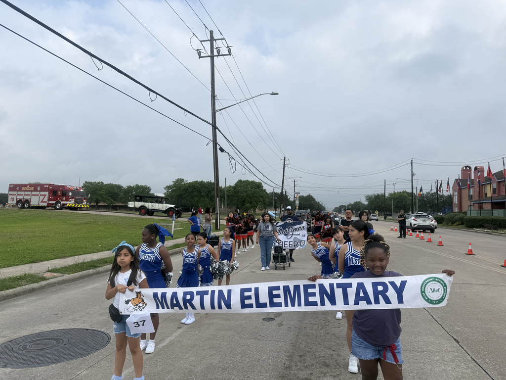 A group of children in blue uniforms walk down a street with a banner reading "MARTIN ELEMENTARY" above them.