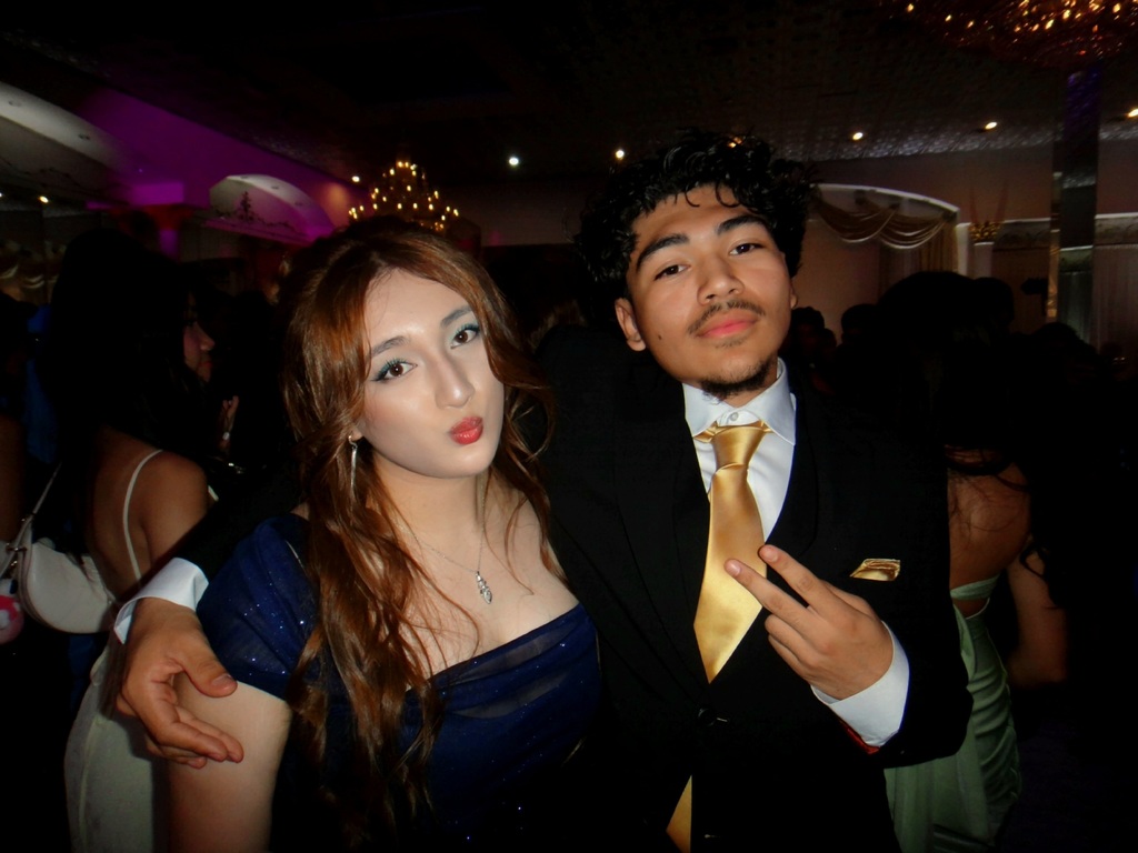 A man and a woman in formal wear pose for a picture in a crowded room.
