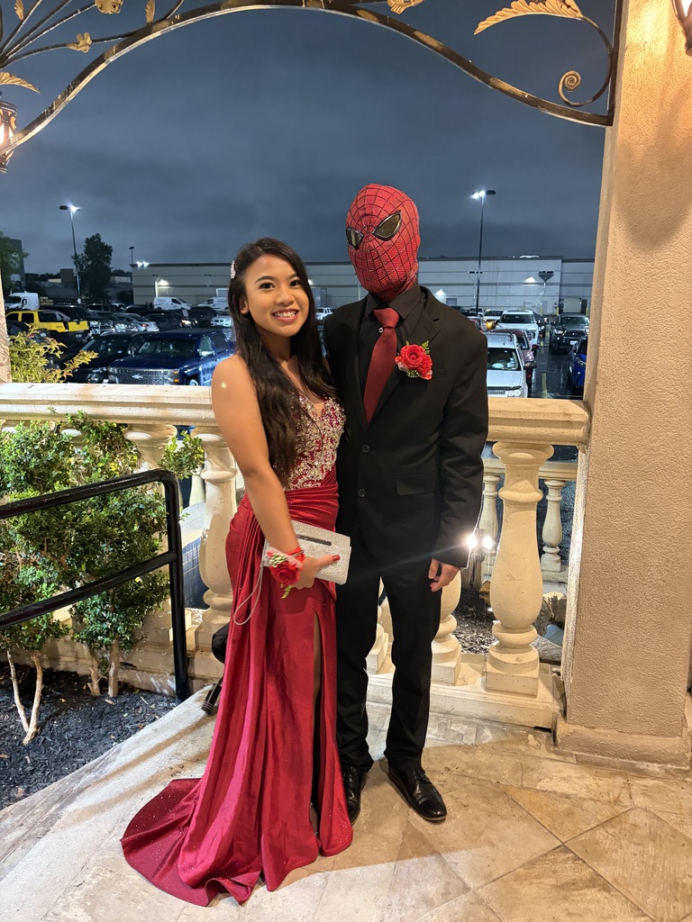 A woman in a red gown and a man in a red mask pose together outside a building at night.