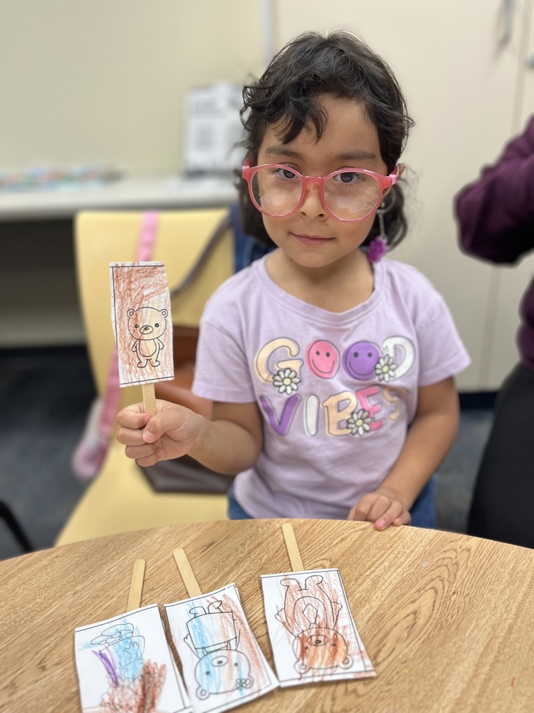 A child holds a small card with a drawing while seated at a table with additional cards.