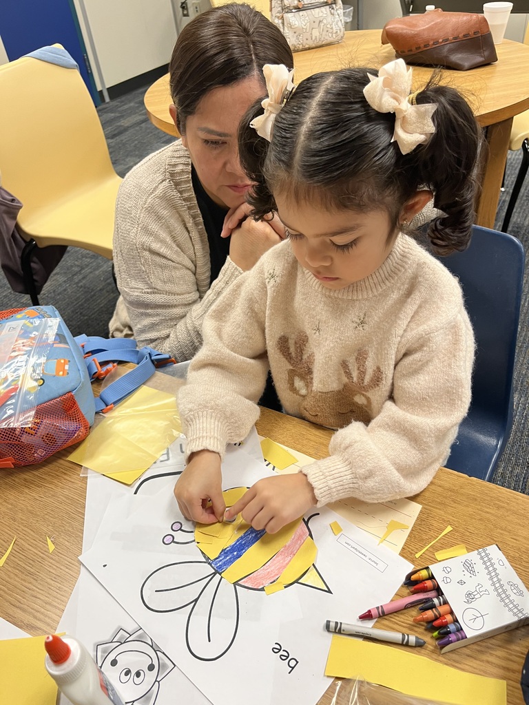 Woman and young girl seated at a table, coloring a large drawing with crayons and markers.
