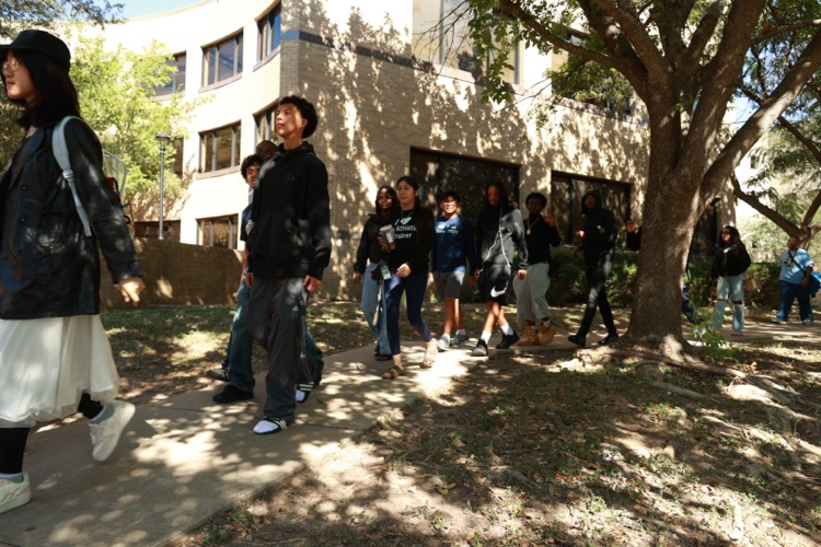 A group of people walking on a path in front of a building. Some wear hats.