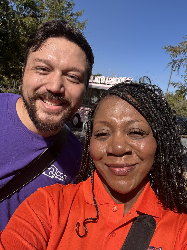Man and woman smile with a food truck, street, and trees in the background.