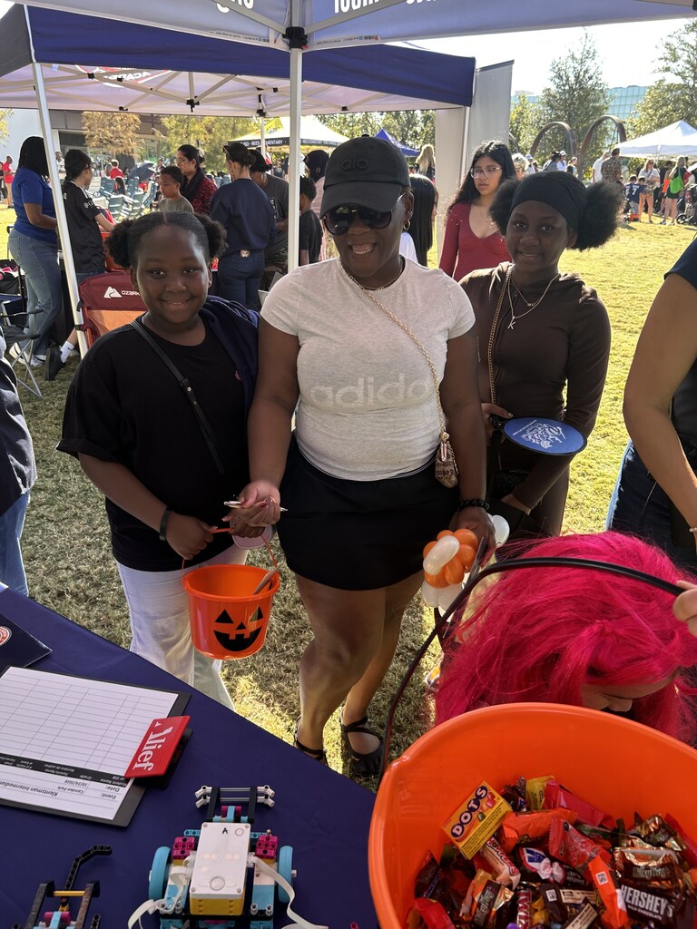 A woman holds a bucket of Halloween candy while standing with two girls at a table.