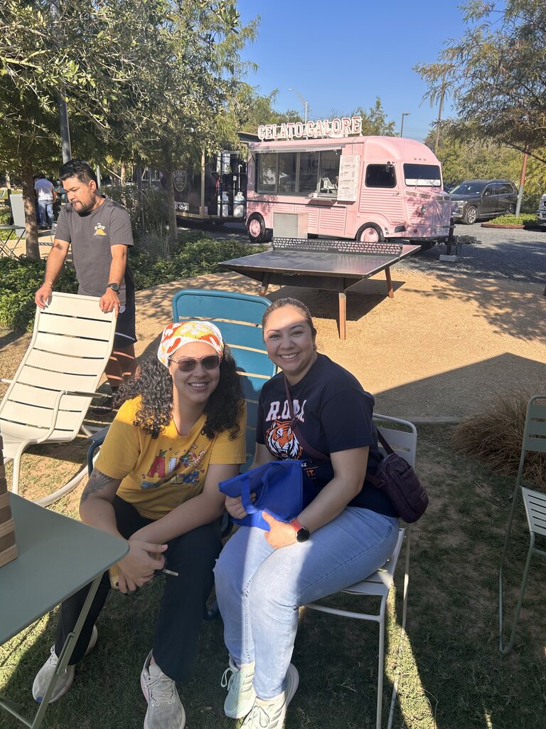 Two women seated in chairs on a lawn. A food truck and other vehicles are in the background.