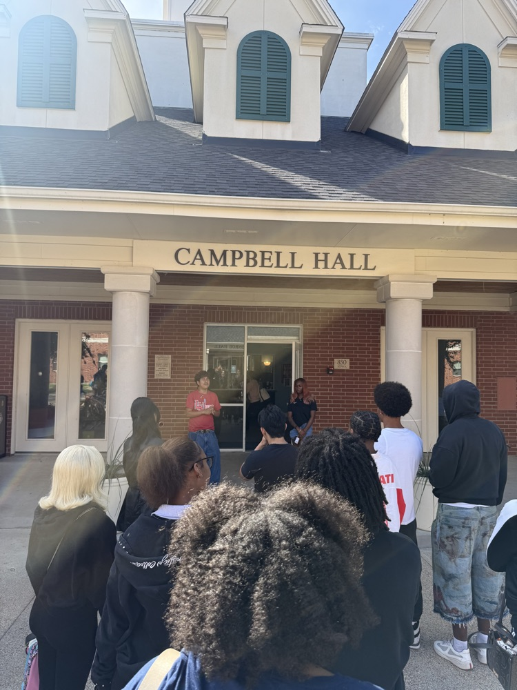 Group of students and adults standing in front of Campbell Hall. One adult wearing a red shirt stands in doorway.