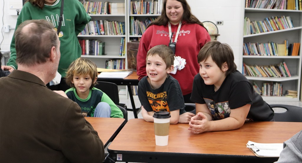 Three young students smile as cartoonist Brad displays his artwork