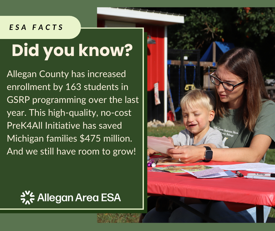A teacher sits at table with a student cutting paper