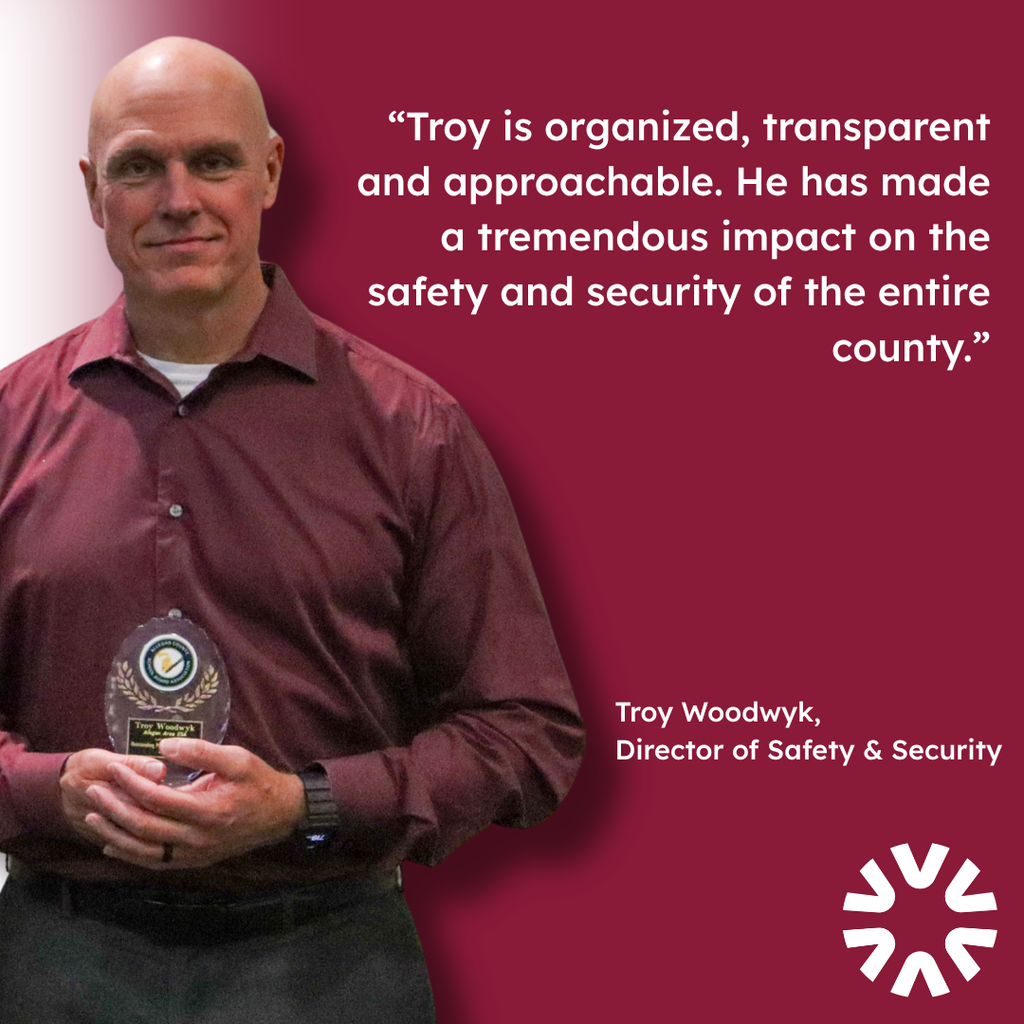 A graphic featuring Troy Woodwyk, Director of Safety & Security, holding an award plaque against a dark red background. The graphic includes the quote: “Troy is organized, transparent and approachable. He has made a tremendous impact on the safety and security of the entire county.” Troy’s name and title appear in the lower right corner alongside the Allegan Area ESA logo.