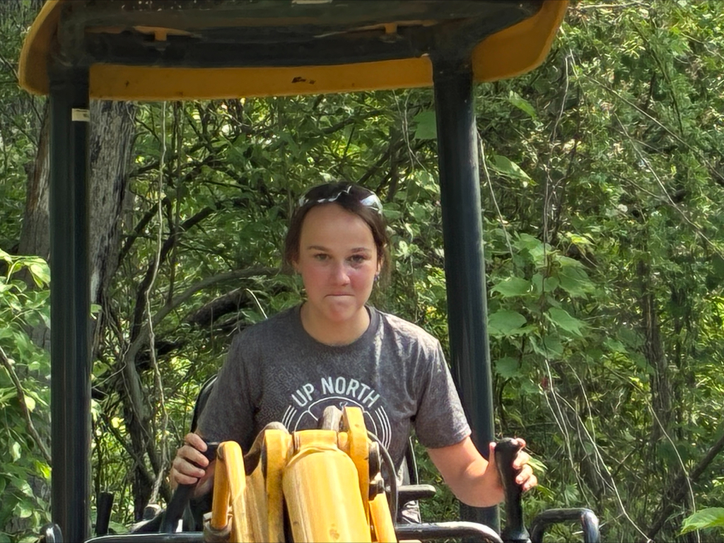 Camper on a yellow Komatsu excavator digging a hole with a look of determination.
