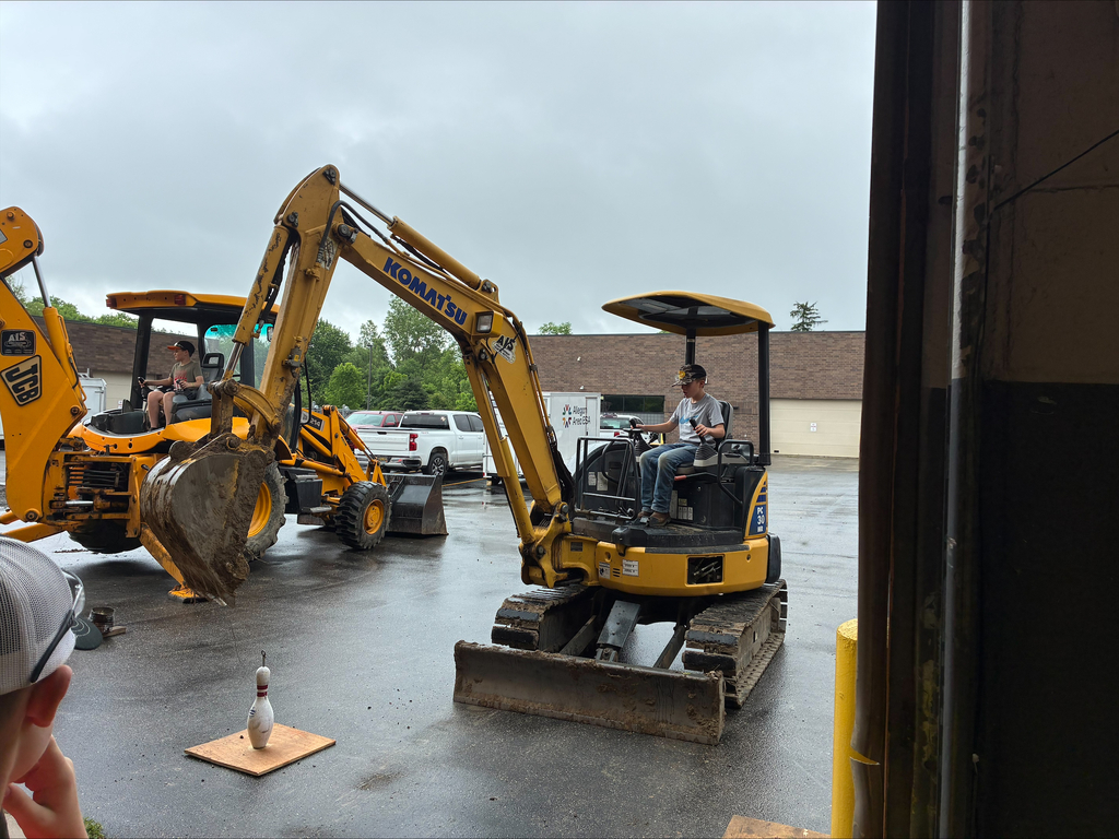 Camper on a yellow Komatsu excavator doing challenge testing and attempting to hook a bowling pin.