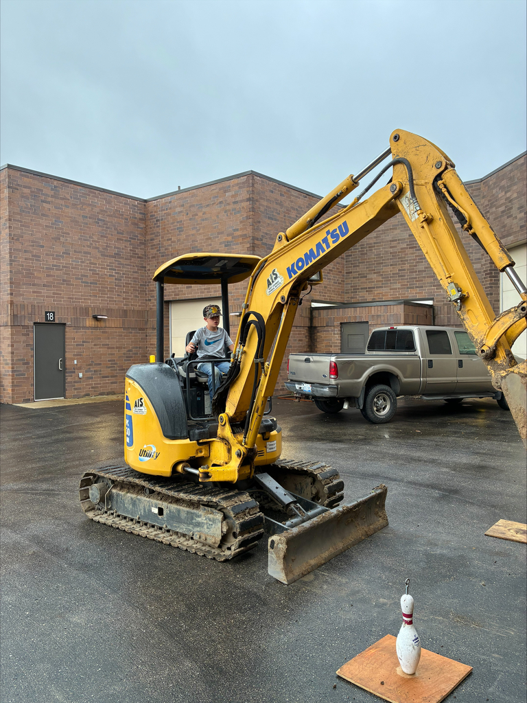 Camper on a yellow Komatsu small excavator attempting to hook a bowling pin.