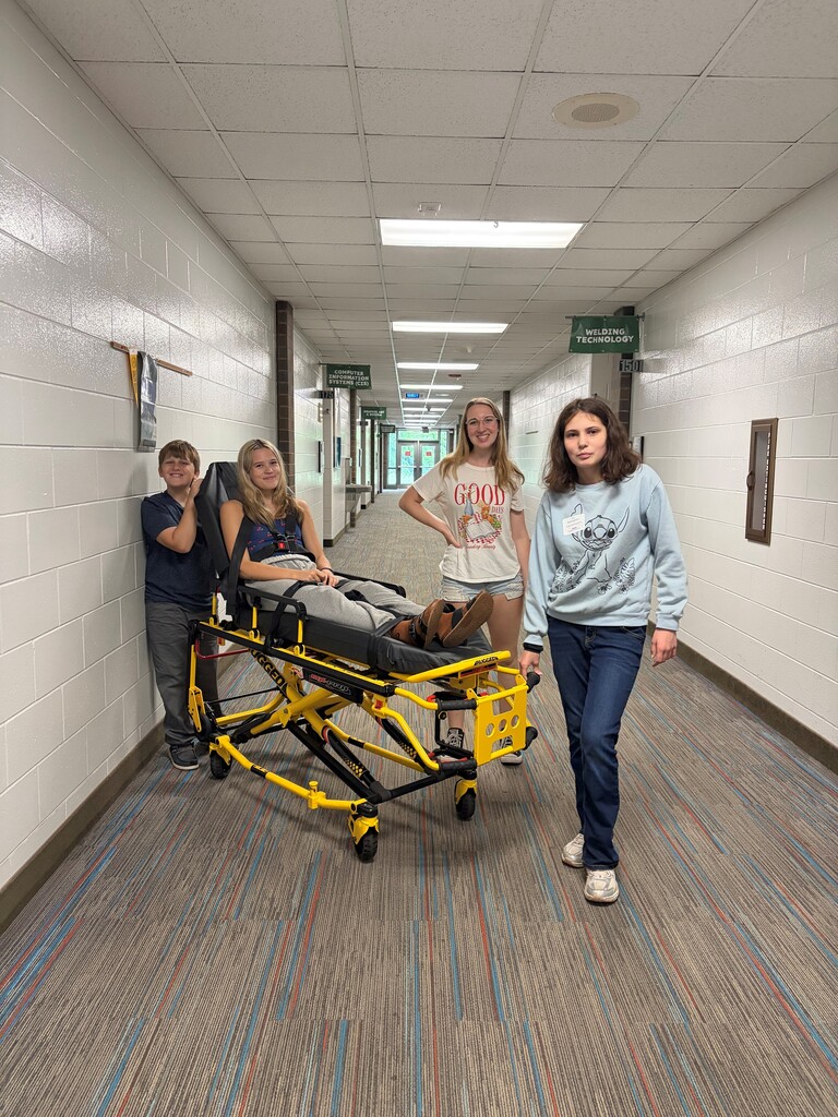 3 campers maneuvering a stretcher with the EMS camp assistant on board.