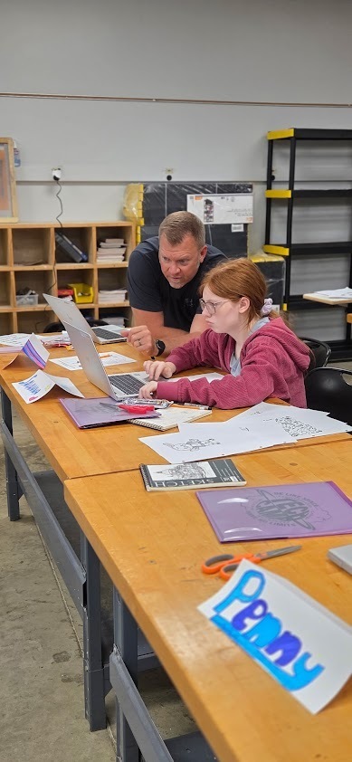 Instructor, Tim Herremans, helps a female camper with her digital design at a laptop