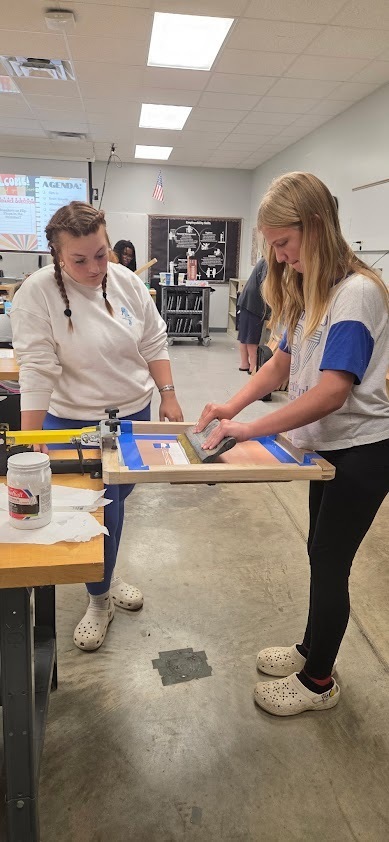 Female student stands at a workstation and pulls ink from screen to shirt