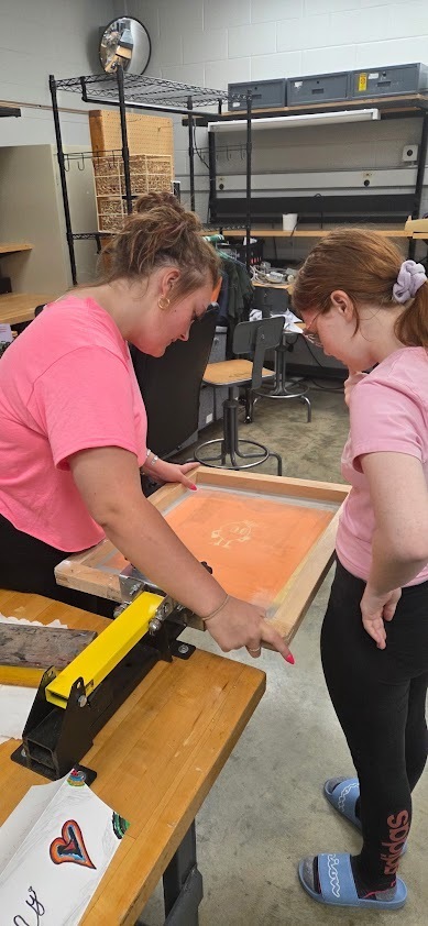 A student volunteer assists a female student on transferring the design to the screen