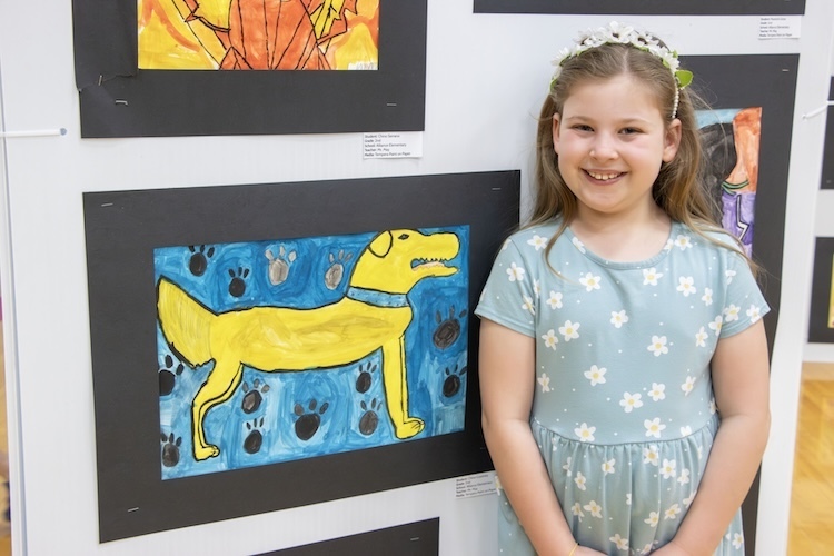 a student smiling while standing by her art work