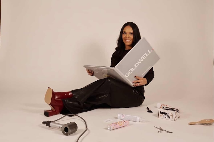 Devin holding a beauty book while sitting on the flour with hair tools around her