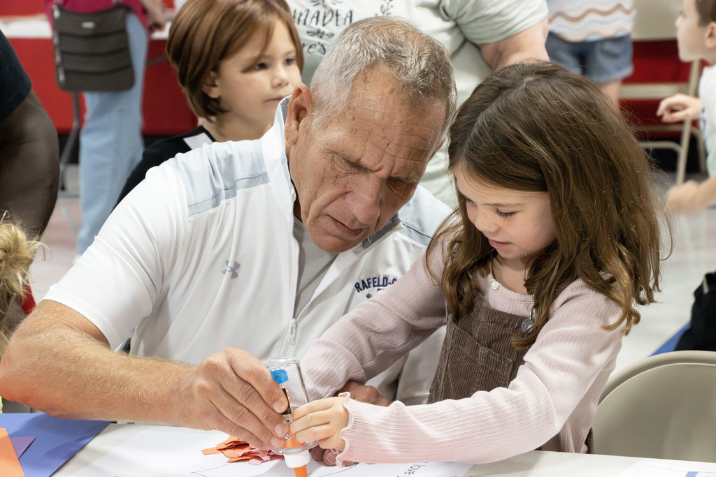 A grandparent helping his granddaughter with glue