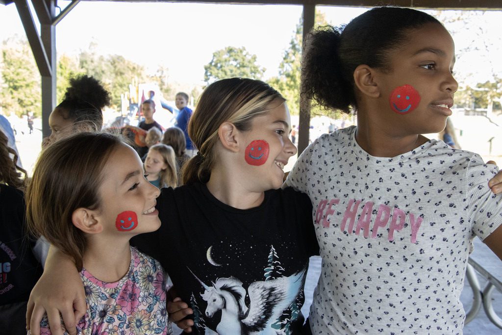 three students smiling with red and blue smiley faces on their cheeks