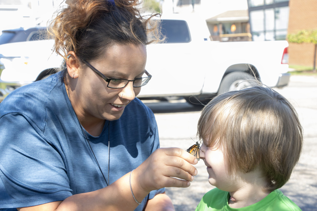 a teacher aide putting a butterfly on a students nose while both smith