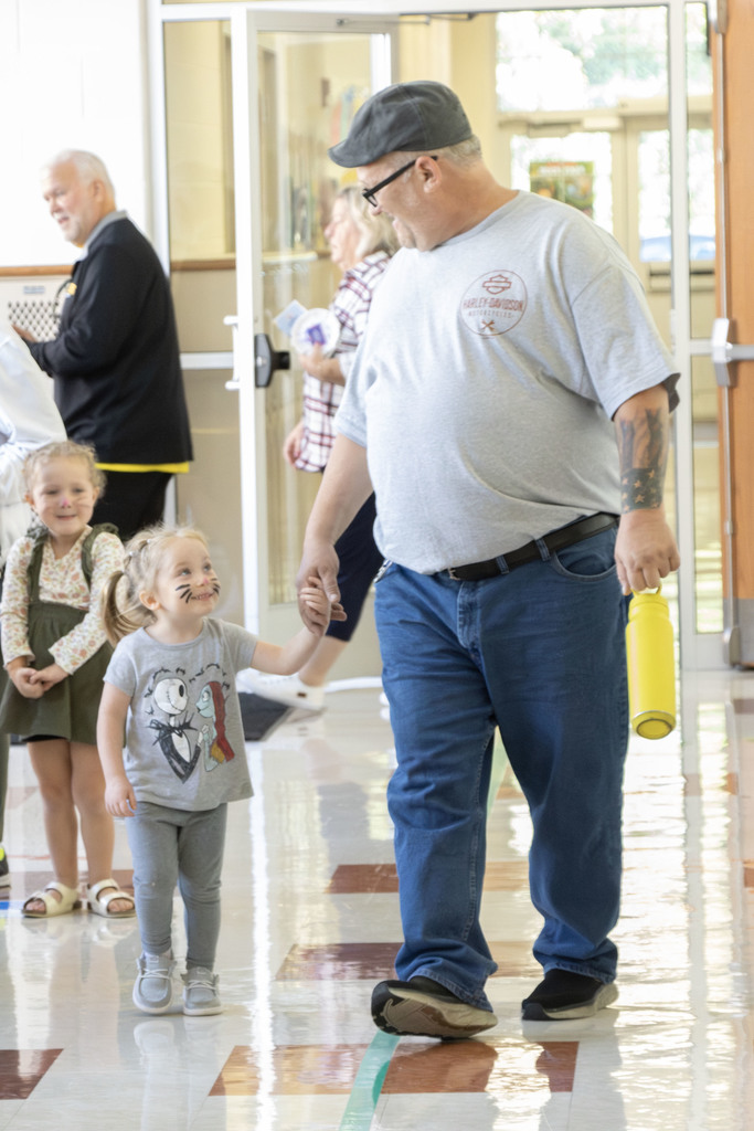 a grandp smiling down at his grand daughter as they walk hand in hand down the hall.