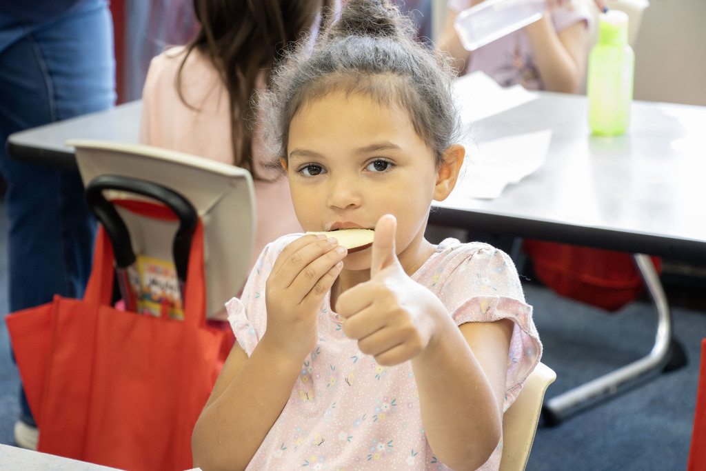 a student giving a thumbs up while eating a slice of apple
