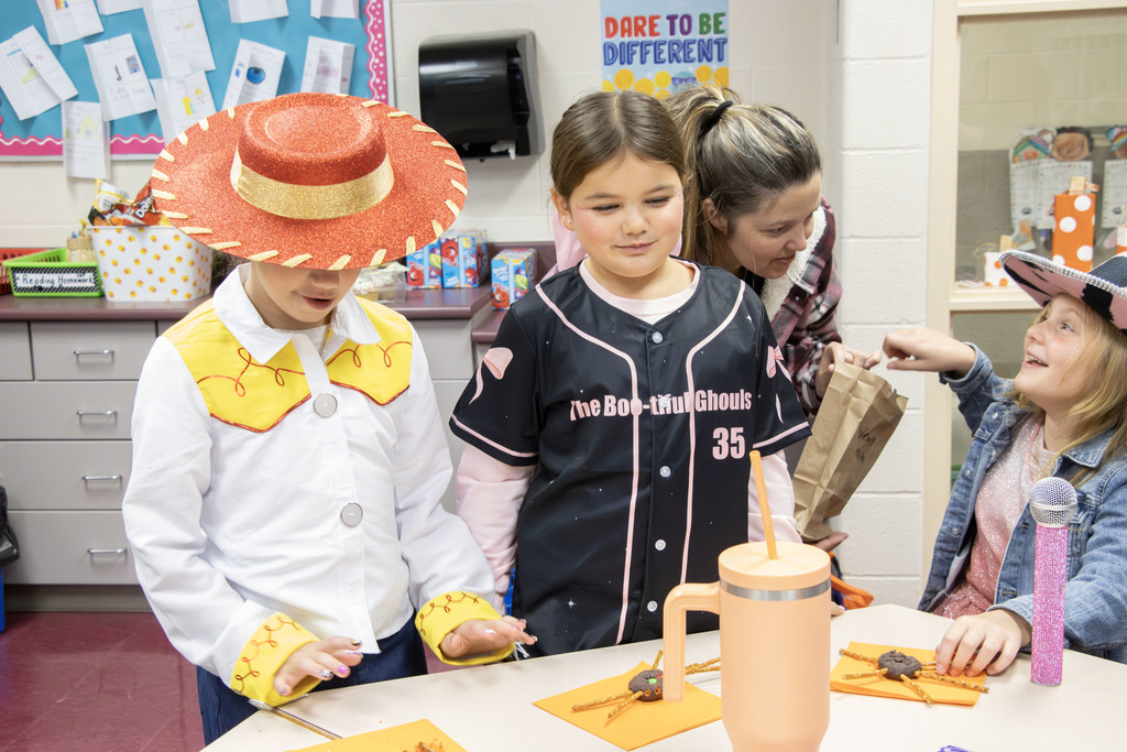 students dressed as Jesse from Toy Story and a softball player make a spider shaped cookie
