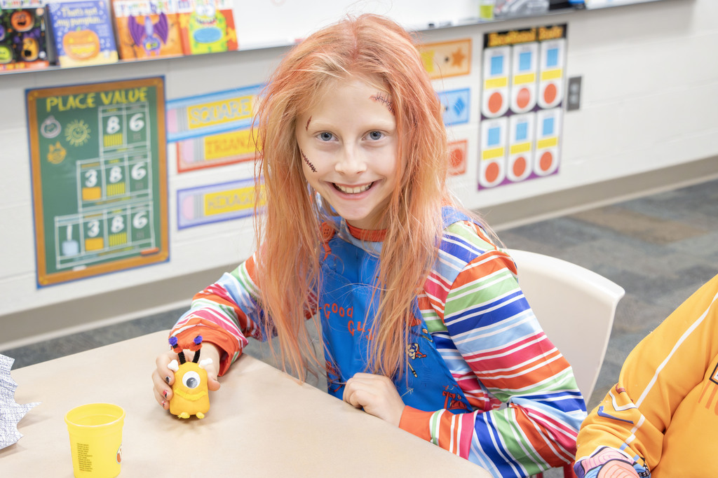 a student dressed as chucky smiles and holds their monster made out of clay