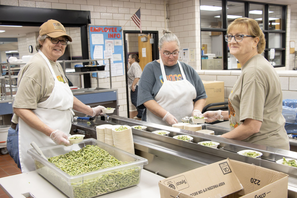 Three cafeteria aides packing green beans